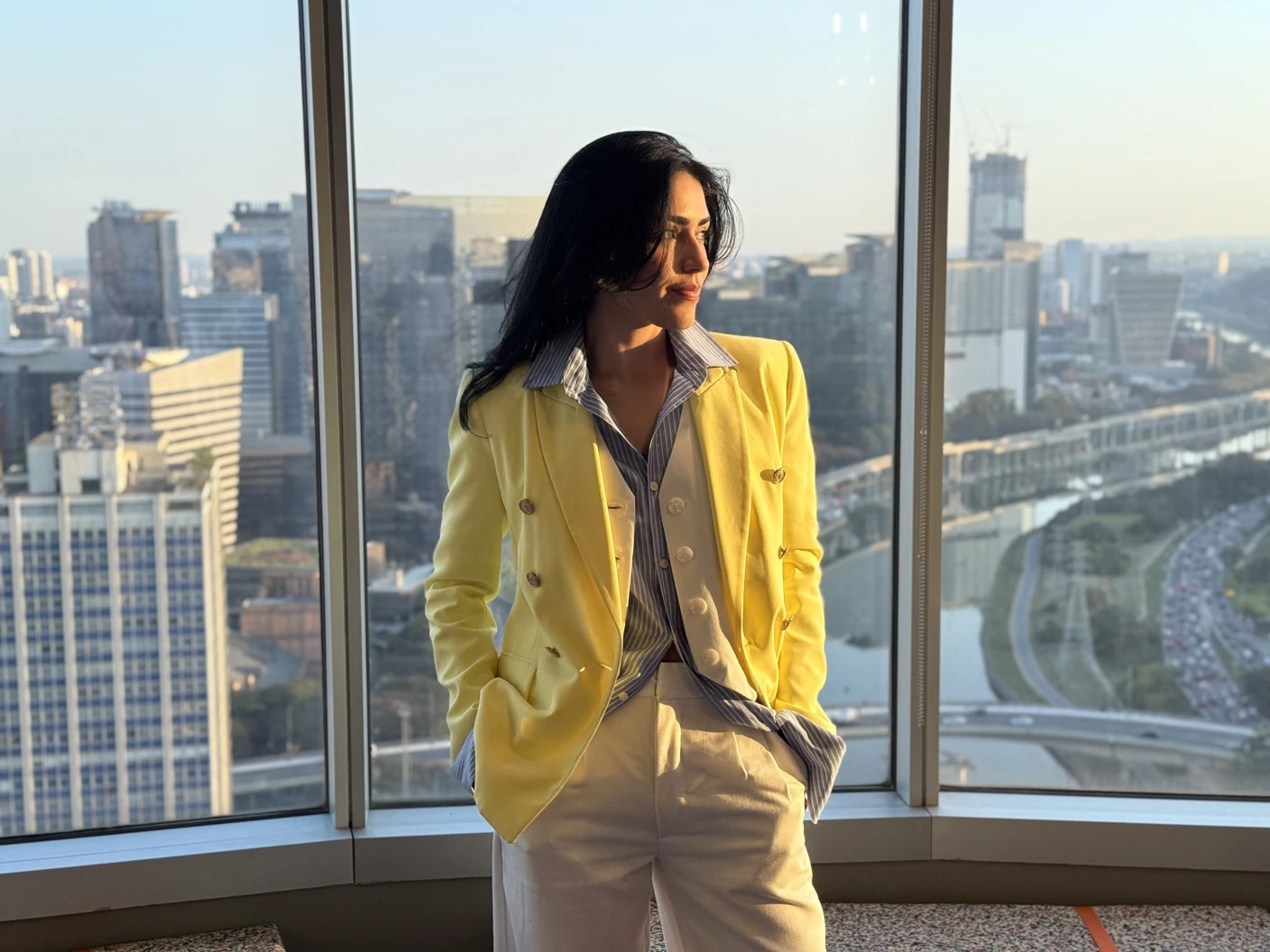 Carla Juliana, de blazer amarelo, junto a uma janela